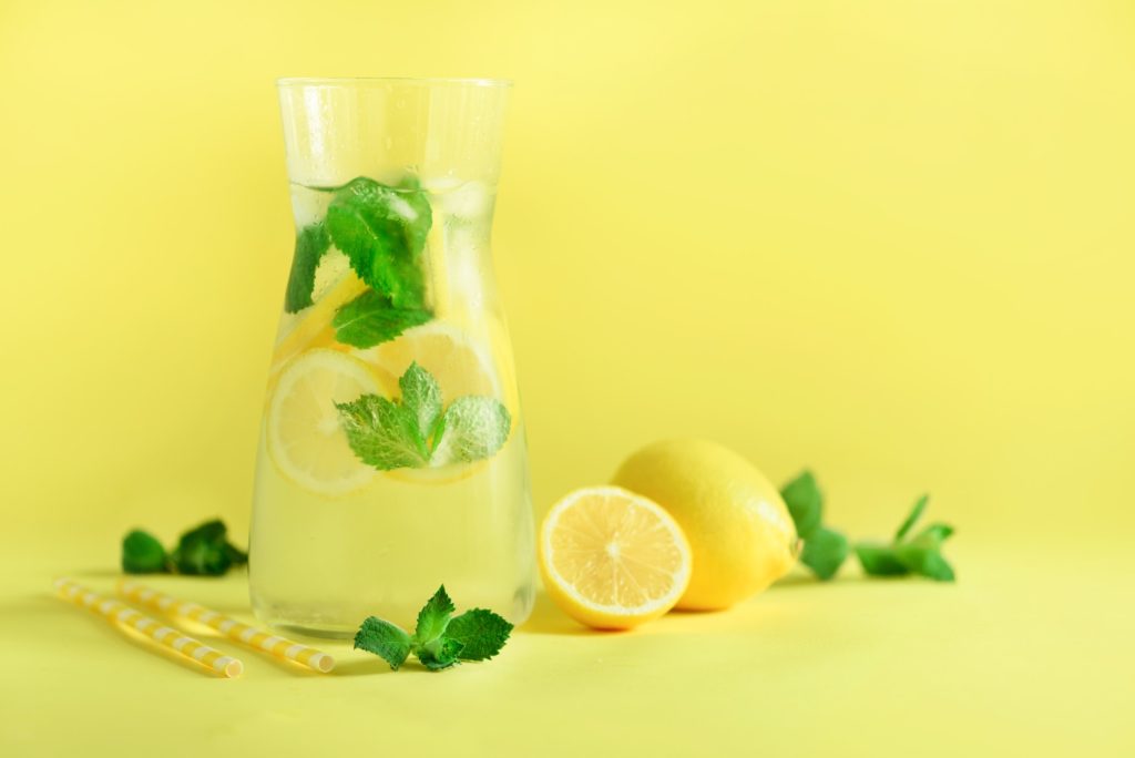 Fresh summer fruits water or lemonade with mint, ice, lemon on yellow background. Copy space. Summer